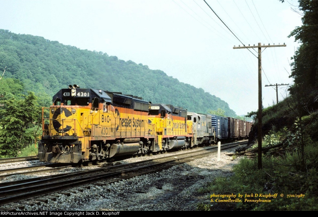 Chessie, B&O GP40-2 4301-C&O GP38 3870-L&N U23B 3298, with eastbound R396. about to head up the Yough gorge and the east slope of Sand Patch grade, at S. Connellsville, Pennsylvania. July 1, 1987. 
